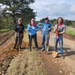 Four college students stand with shovels by road.