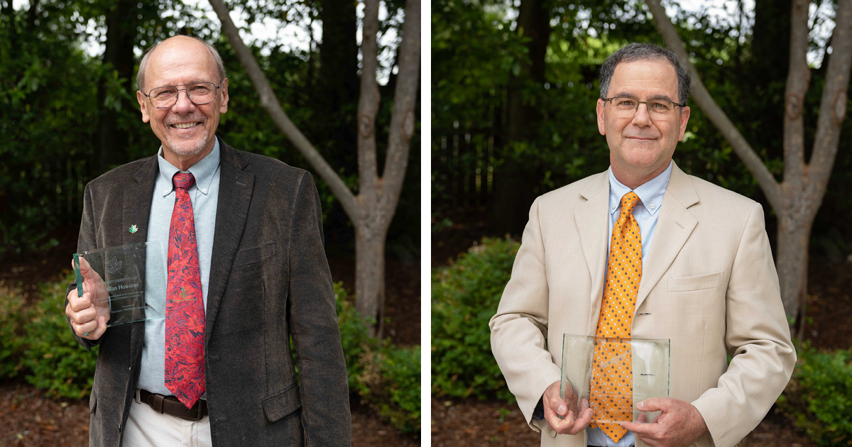 Two men smile in front of tree