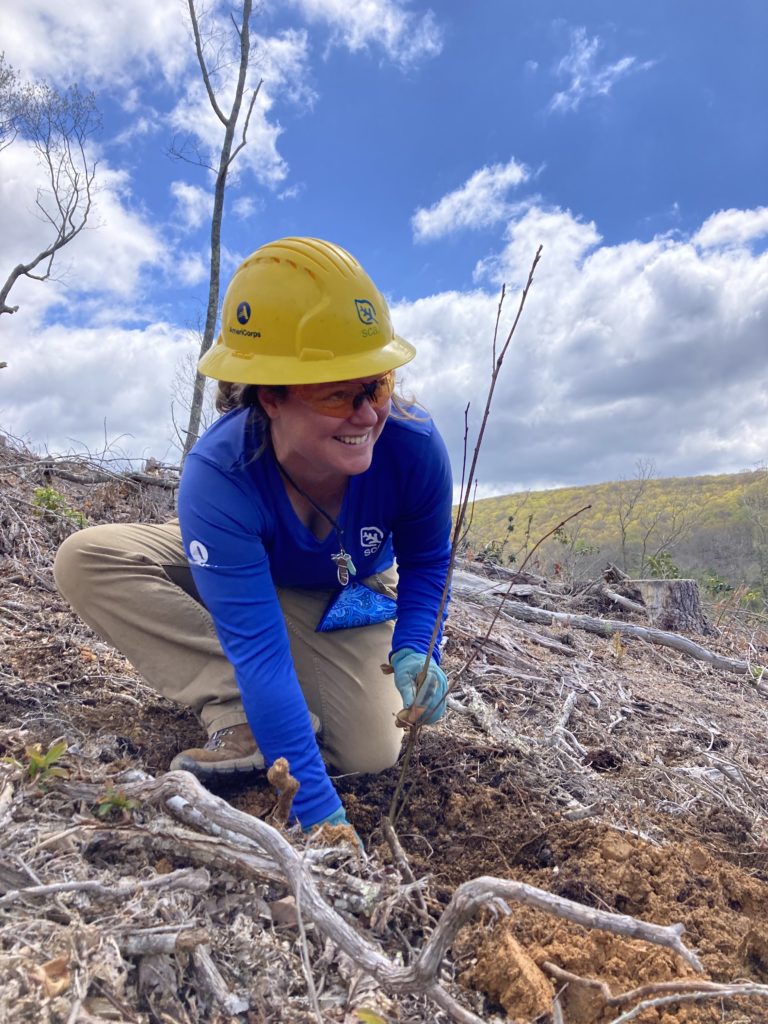 Woman smiles while digging in hole.