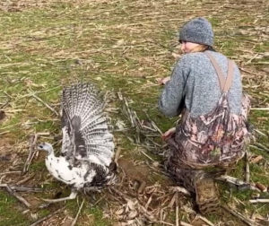 Woman crouches beside wild turkey.