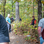 Man talks in a wooded area to group of people.