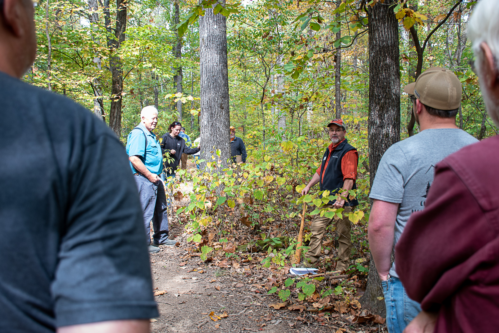 Man talks in a wooded area to group of people.