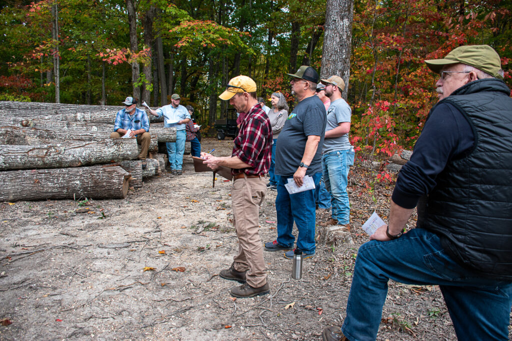 A group of people stands in a wooded area near some logs.