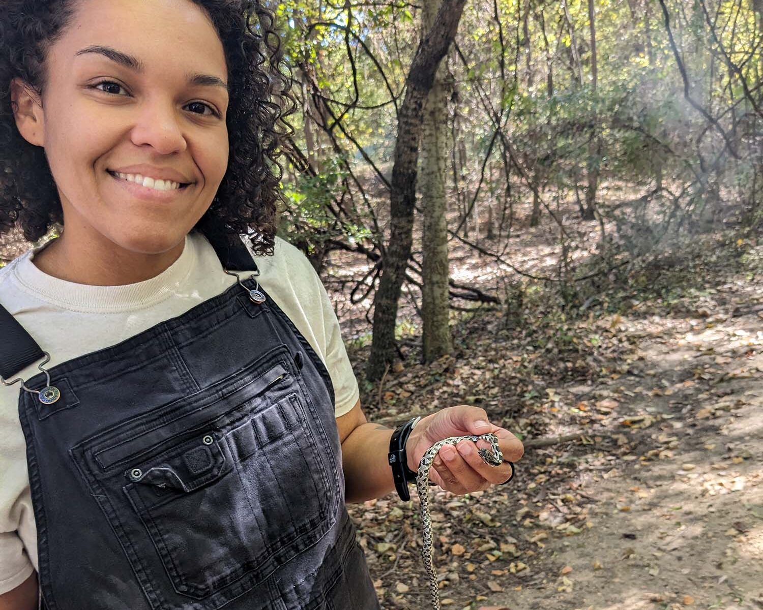 Woman holds small snake in a wooded area.