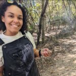 Woman holds small snake in a wooded area.