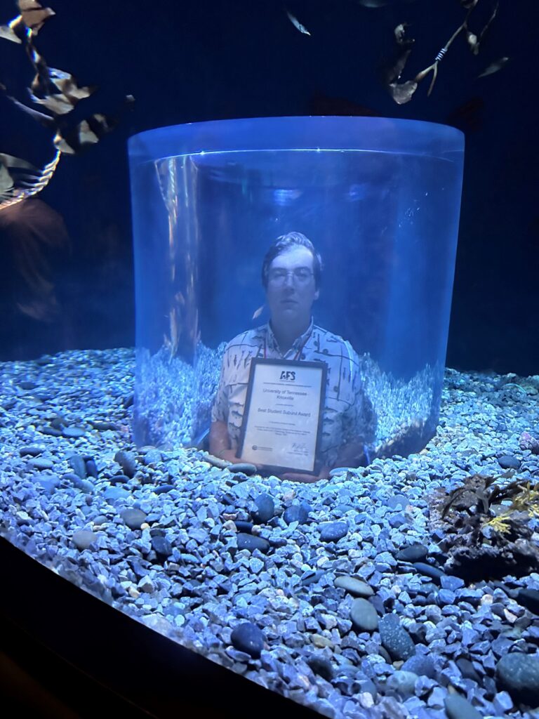 Man holds award while standing in tunnel under aquarium.