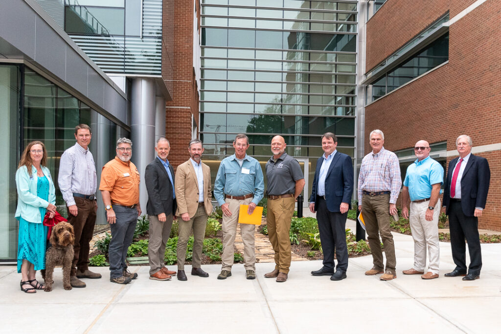 Eleven people stand in a row outside a building with a dog.