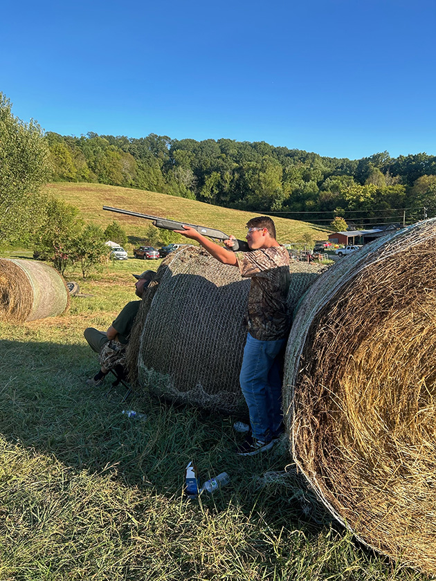 One person points a gun next to a hay bale.