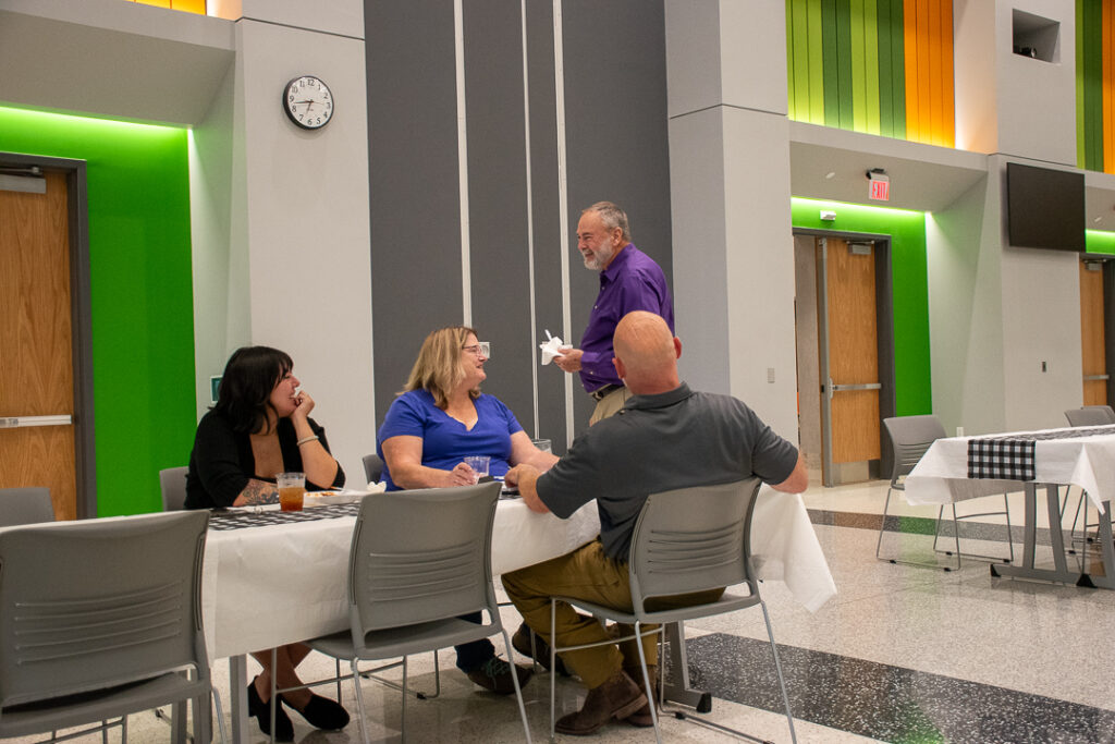 Three people sit and another person stands at a table.