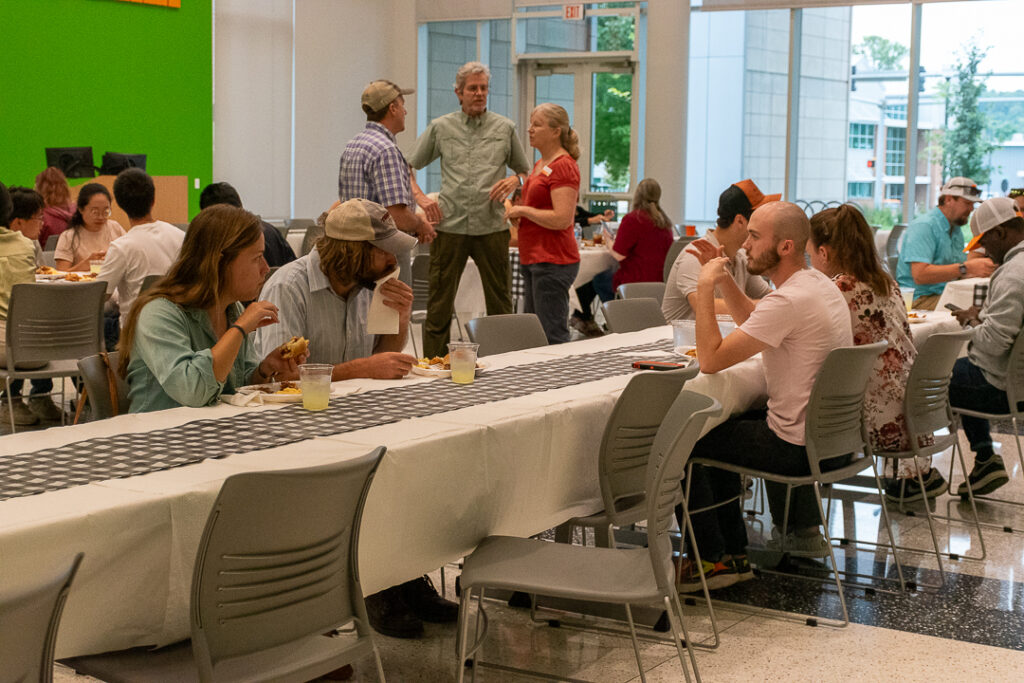 People sit and stand at tables while talking and eating inside a building.