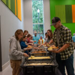 People form two lines around a buffet table to get food.