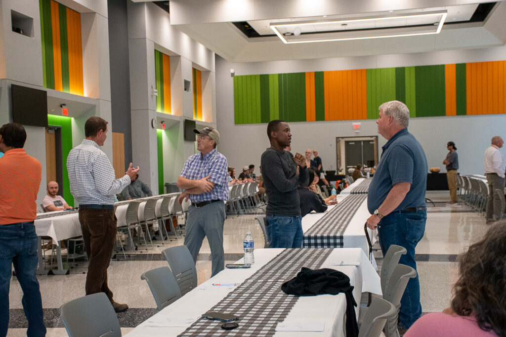 Five people stand and talk around tables.