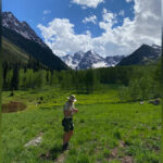 Man in forest ranger uniform looks at something in his hand while standing in a meadow in the mountains.