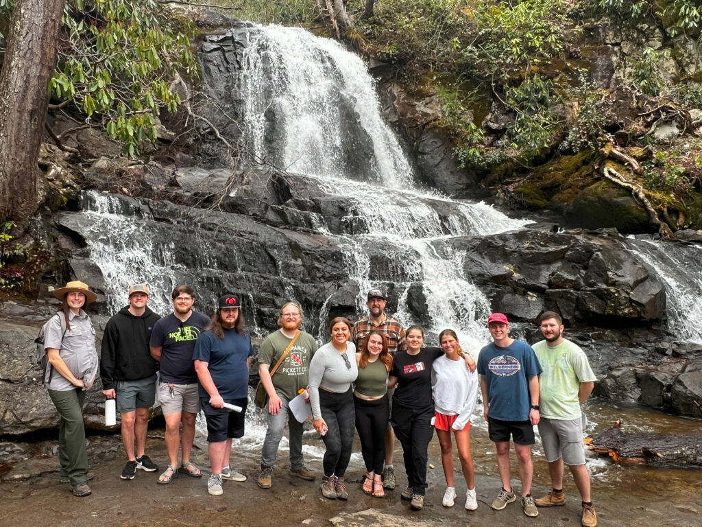 Twelve people stand in front of a waterfall.