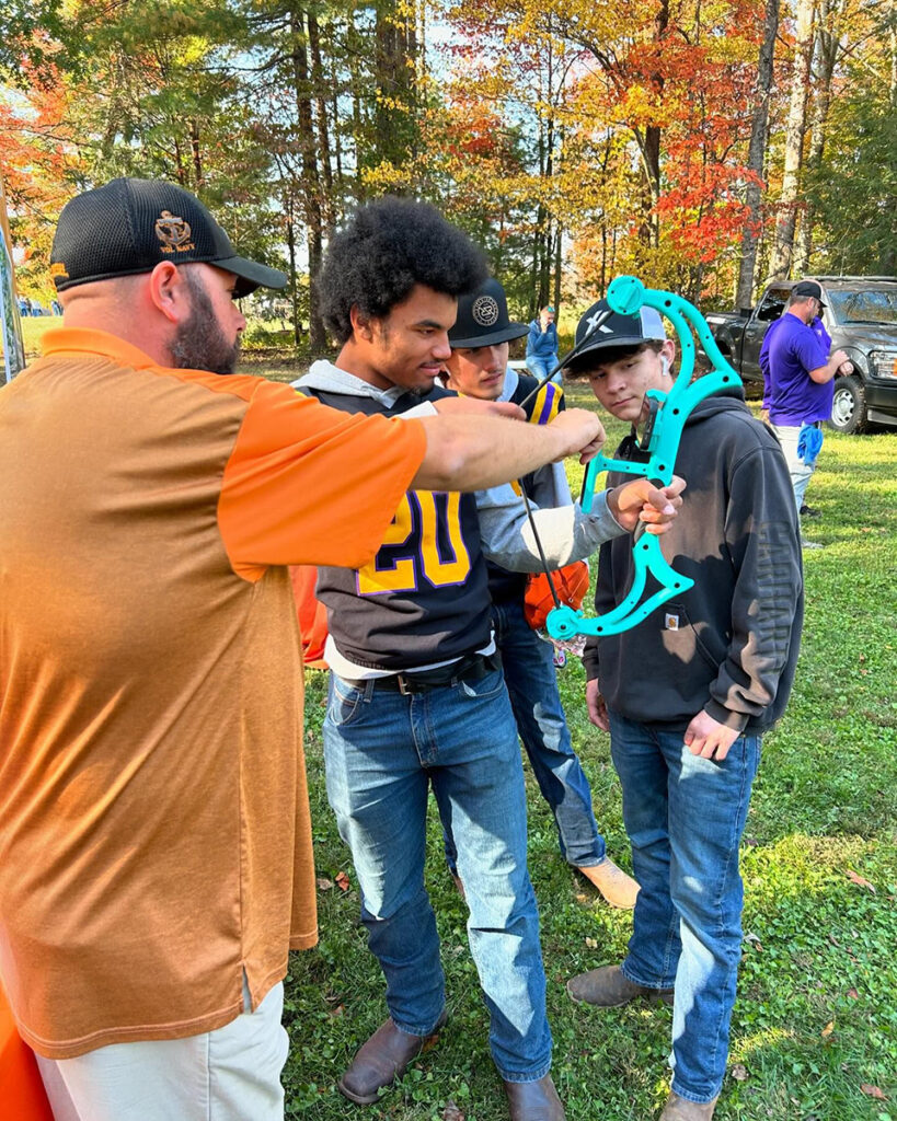 A man instructs two students on holding a hunting bow.