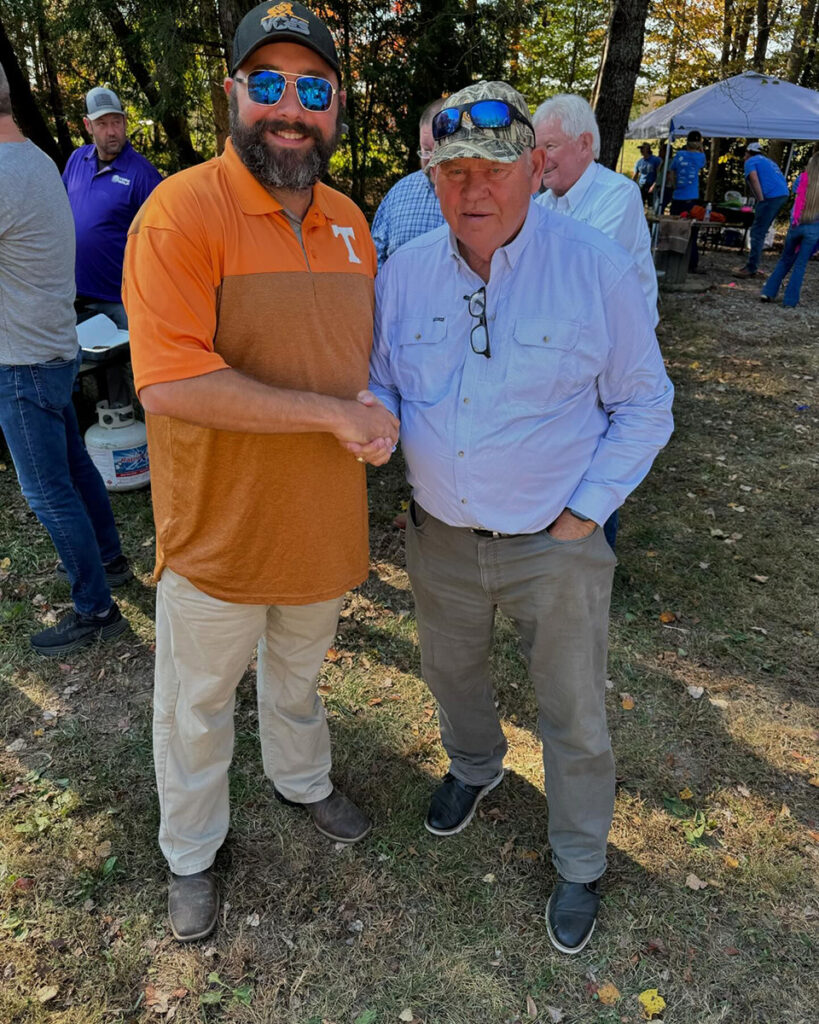 Two men shake hands and smile.