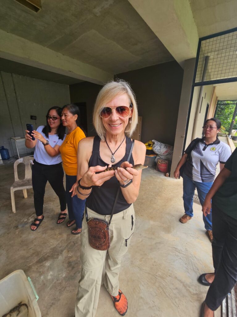 A person holds a young crocodile while other people stand nearby.