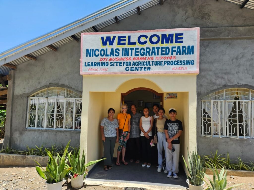 Seven people stand under a welcome sign for a farm.