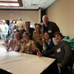 Seven people pose behind a table in a room.