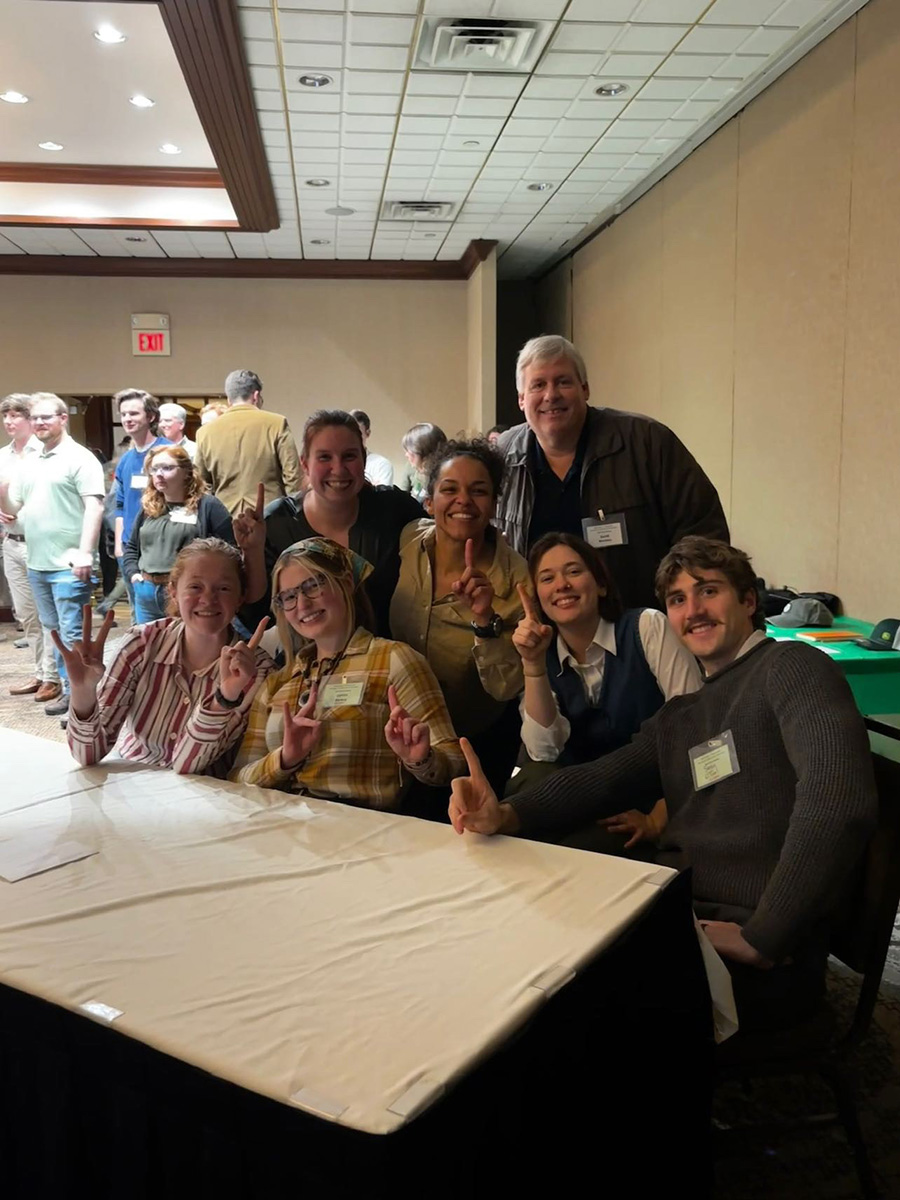 Seven people pose behind a table in a room.