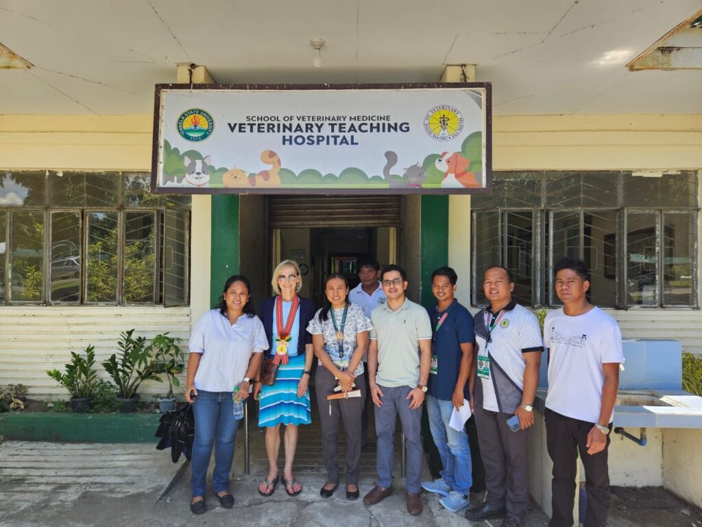 Eight people stand underneath a sign for a veterinary learning hospital.