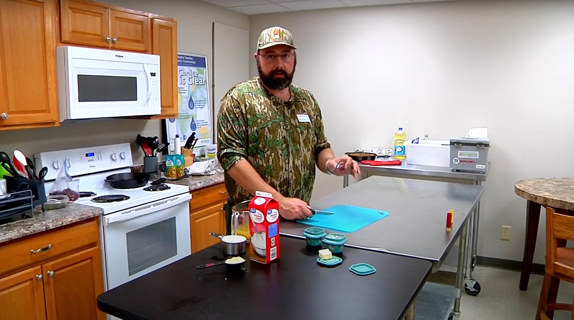 Man stands in kitchen next to table with ingredients and cutting board.