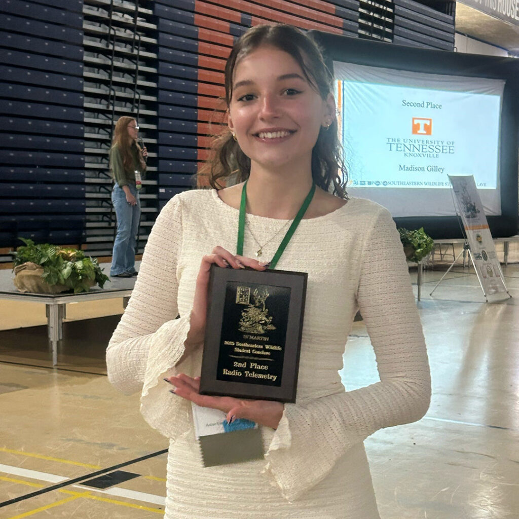 A person in a white dress holds a plaque.