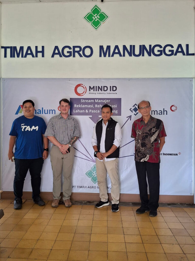 Four people stand and smile under a sign for "Timah Agro Manunggal."