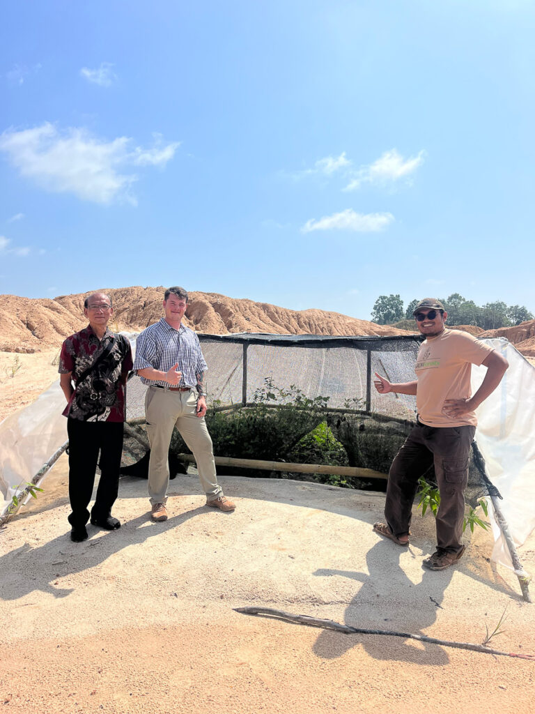 Three people stand next to a plant growth project.