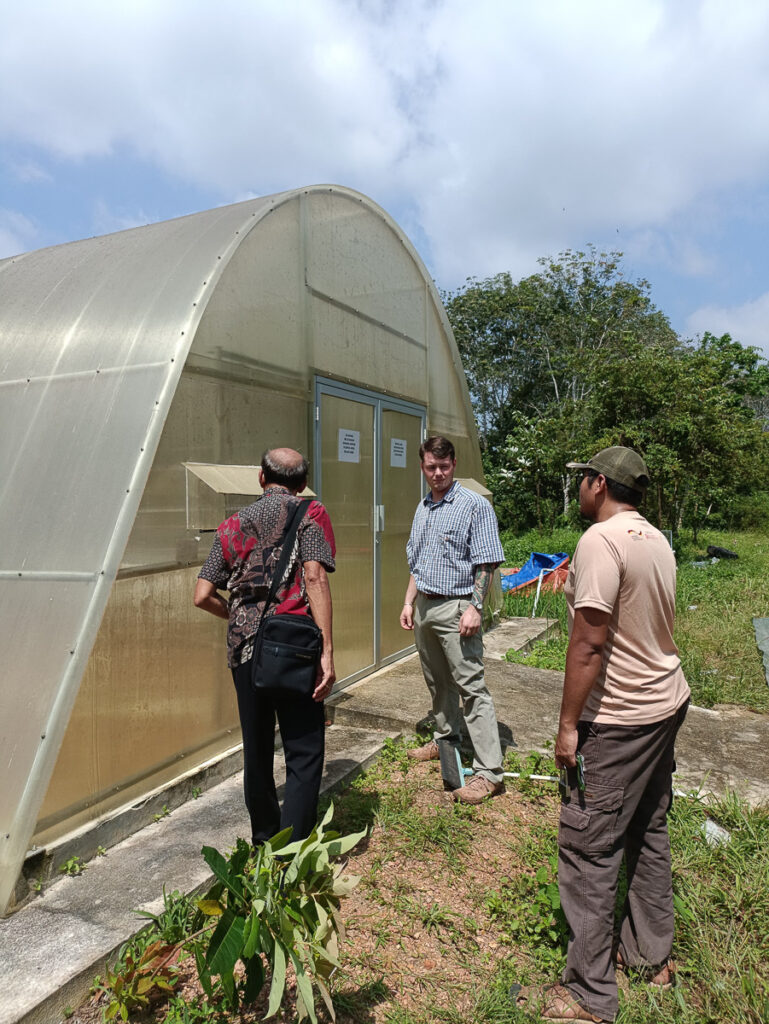 Three people stand outside a greenhouse.