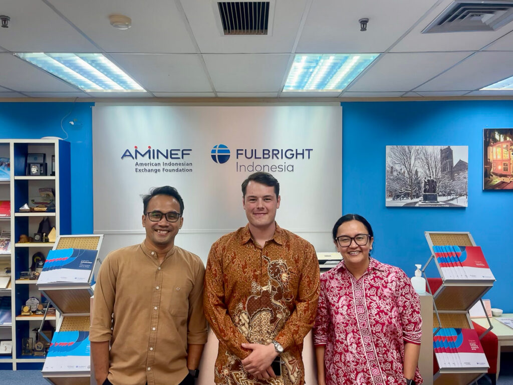 Three people stand in front of a sign for the American Indonesian Exchange Foundation.