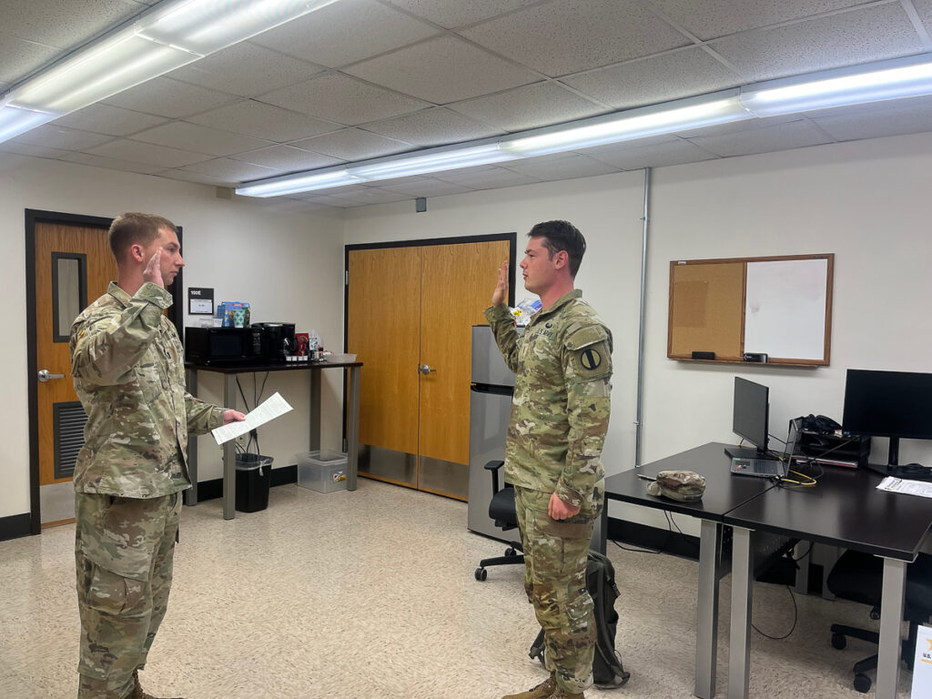 Two people in military uniform hold up their one hand in a room.
