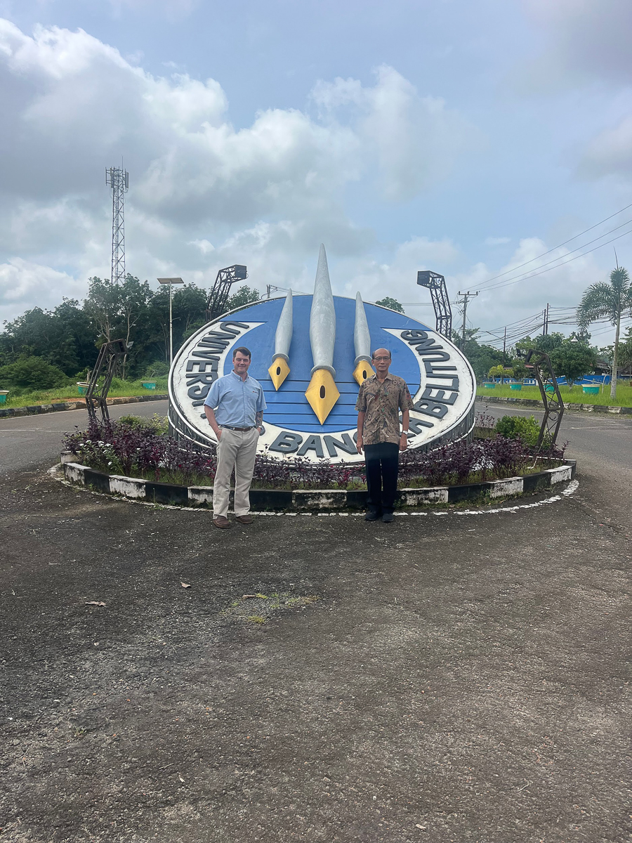 Two people stand in front of the University of Bangka Belitung sign.
