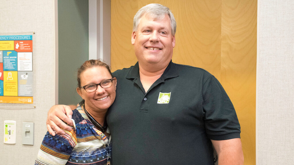 Two people stand next to each other smiling in a room.