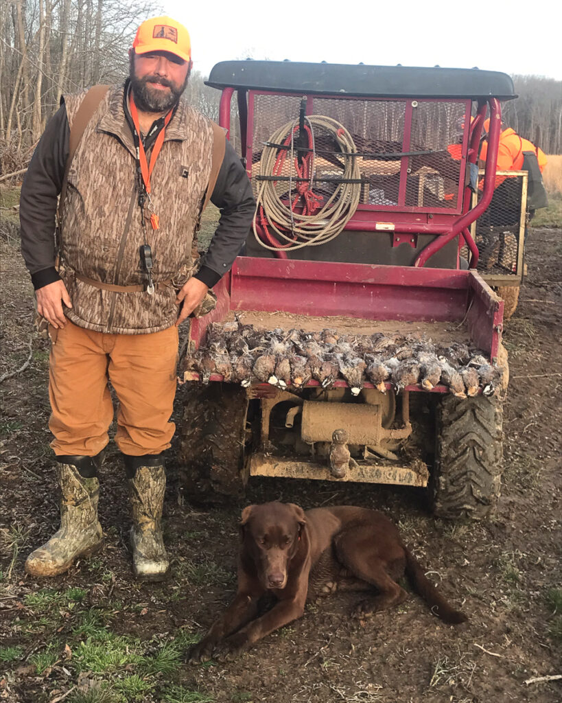 A person smiles next to a dog and dead birds in an all-terrain vehicle.