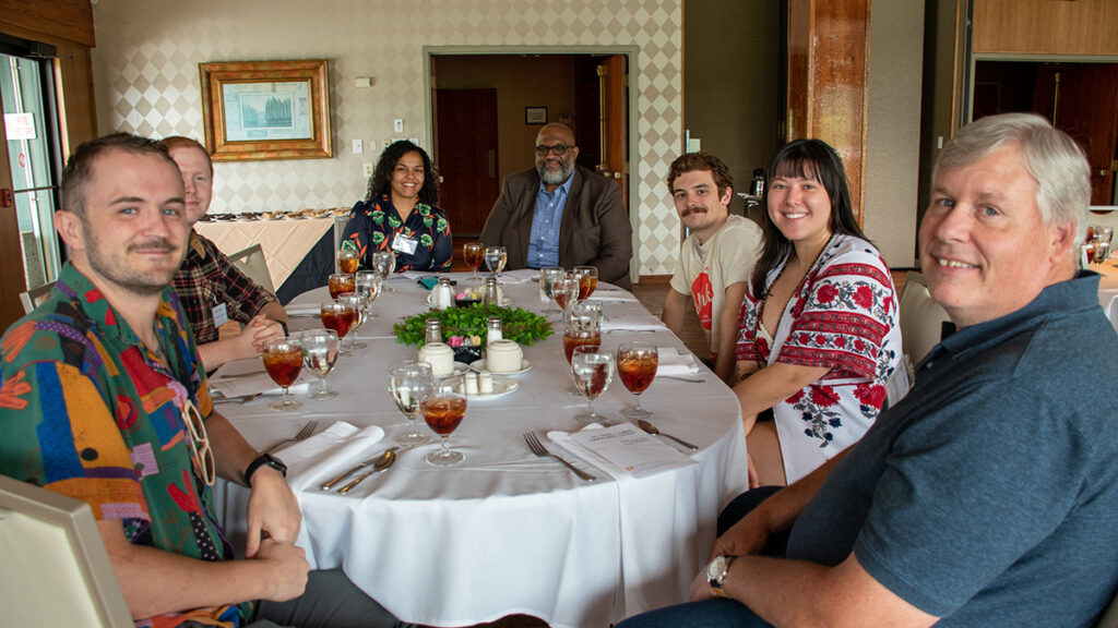 Seven people sit around a table with beverages on it.