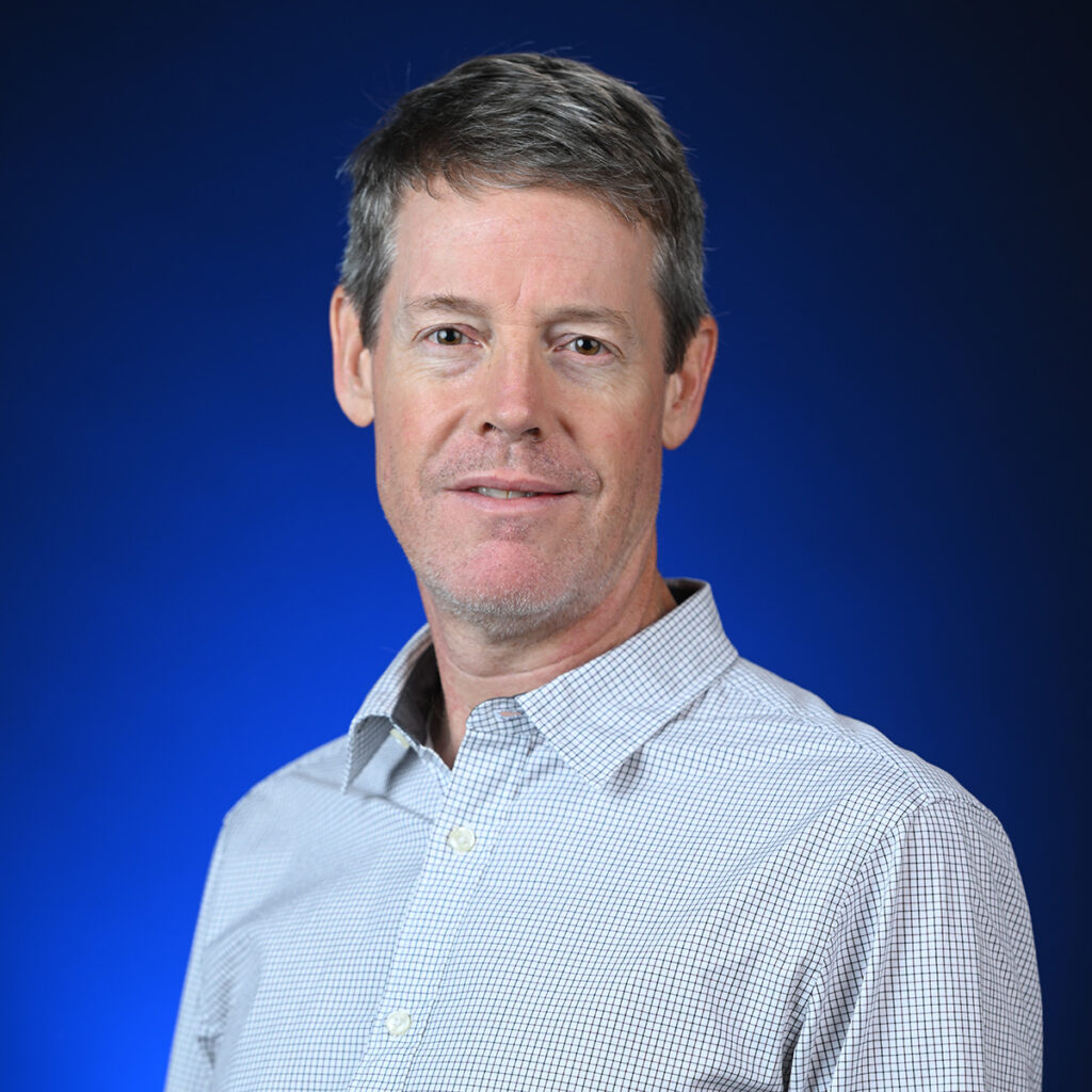 Person in blue and white gingham button up stands in front of blue background.