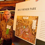 Person wearing name tag stands next to rendering of park named after Billy Minser.