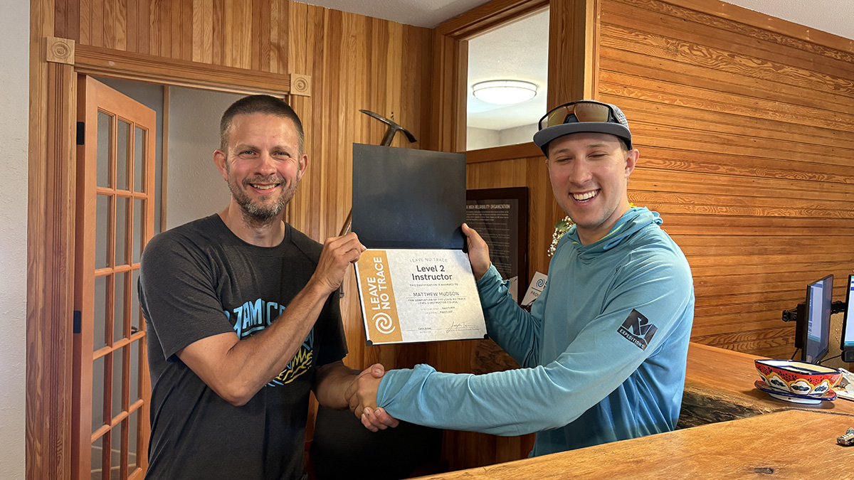 One person shakes another person's hand while holding a certificate.