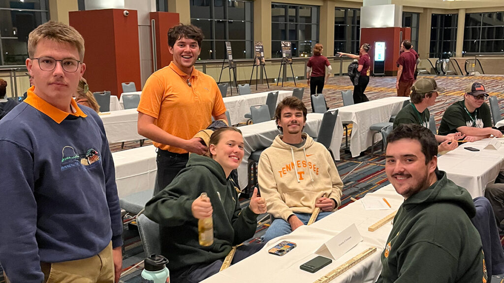 Seven people sit or stand around tables at the Society of American Foresters annual convention.
