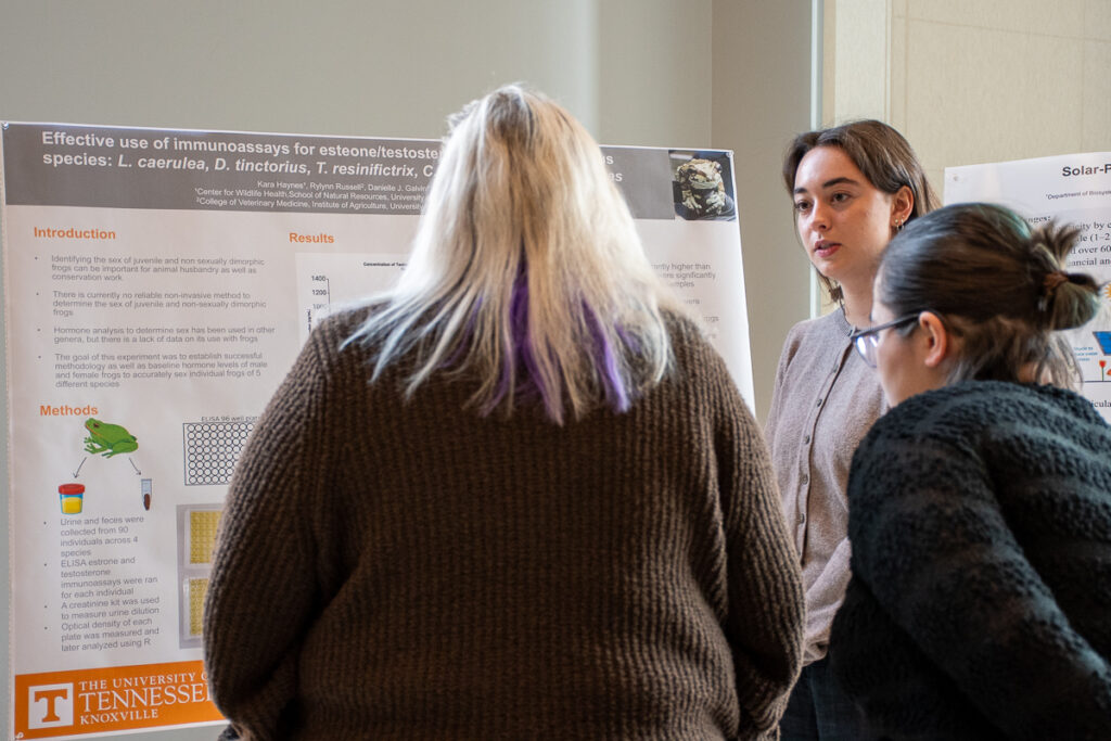 Three people stand in front of a poster on a stand in the Agriculture and Natural Resources Building at the UT Institute of Agriculture.