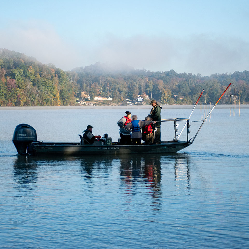 One person sits and four others stand on a boat in Fort Loudoun Lake. 