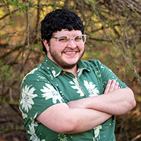 Person stands with arms crossed in front of a tree.