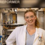 Person wearing lab coat and safety glasses stands in a lab in the Center for Renewable Carbon on the UT Institute of Agriculture.