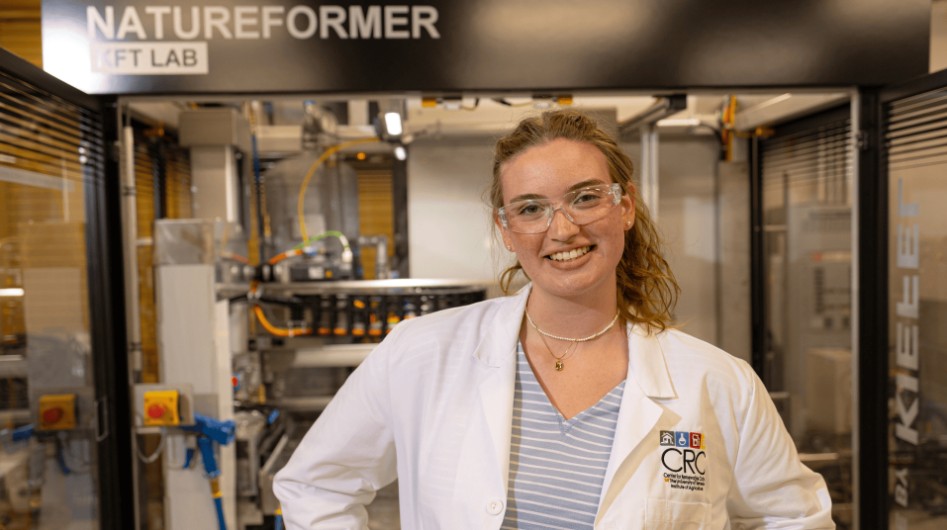 Person wearing lab coat and safety glasses stands in a lab in the Center for Renewable Carbon on the UT Institute of Agriculture.