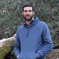 Person stands in front of a bush and rock.