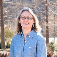 Person smiles in front of trees and grass.
