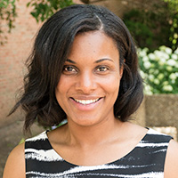 Person stands in front of building and bush.