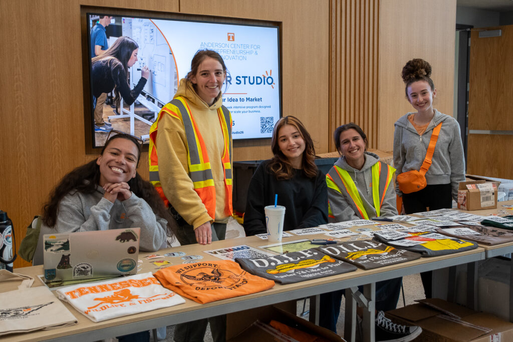 Five people smile behind a table with t-shirts in a building on the UT Institute of Agriculture campus.