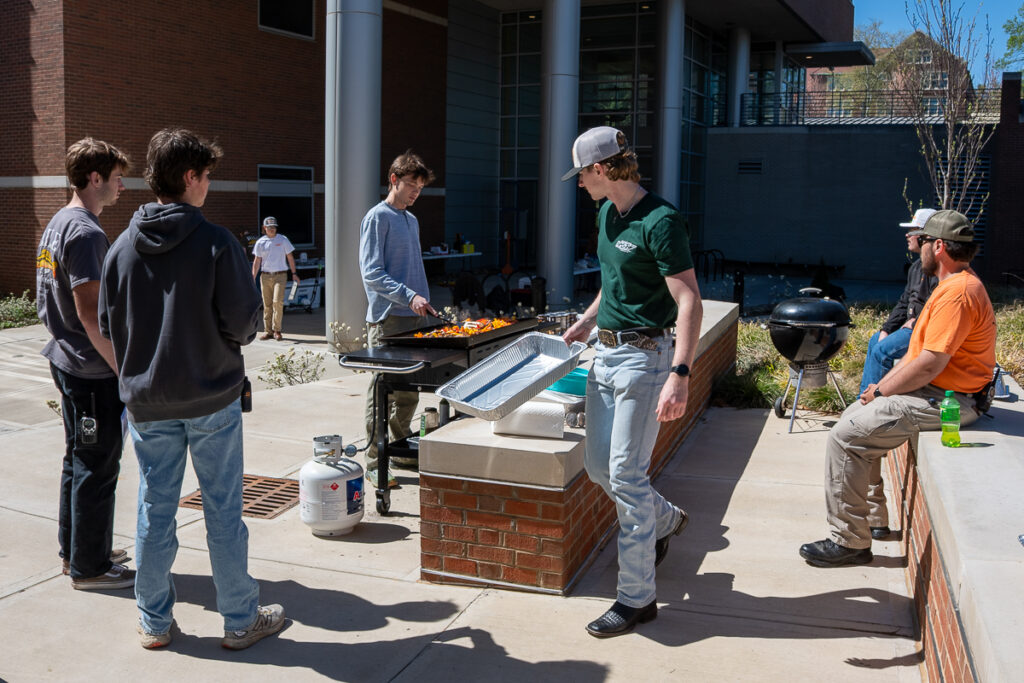 Five people stand around a grill outside a building on the UT Institute of Agriculture campus.